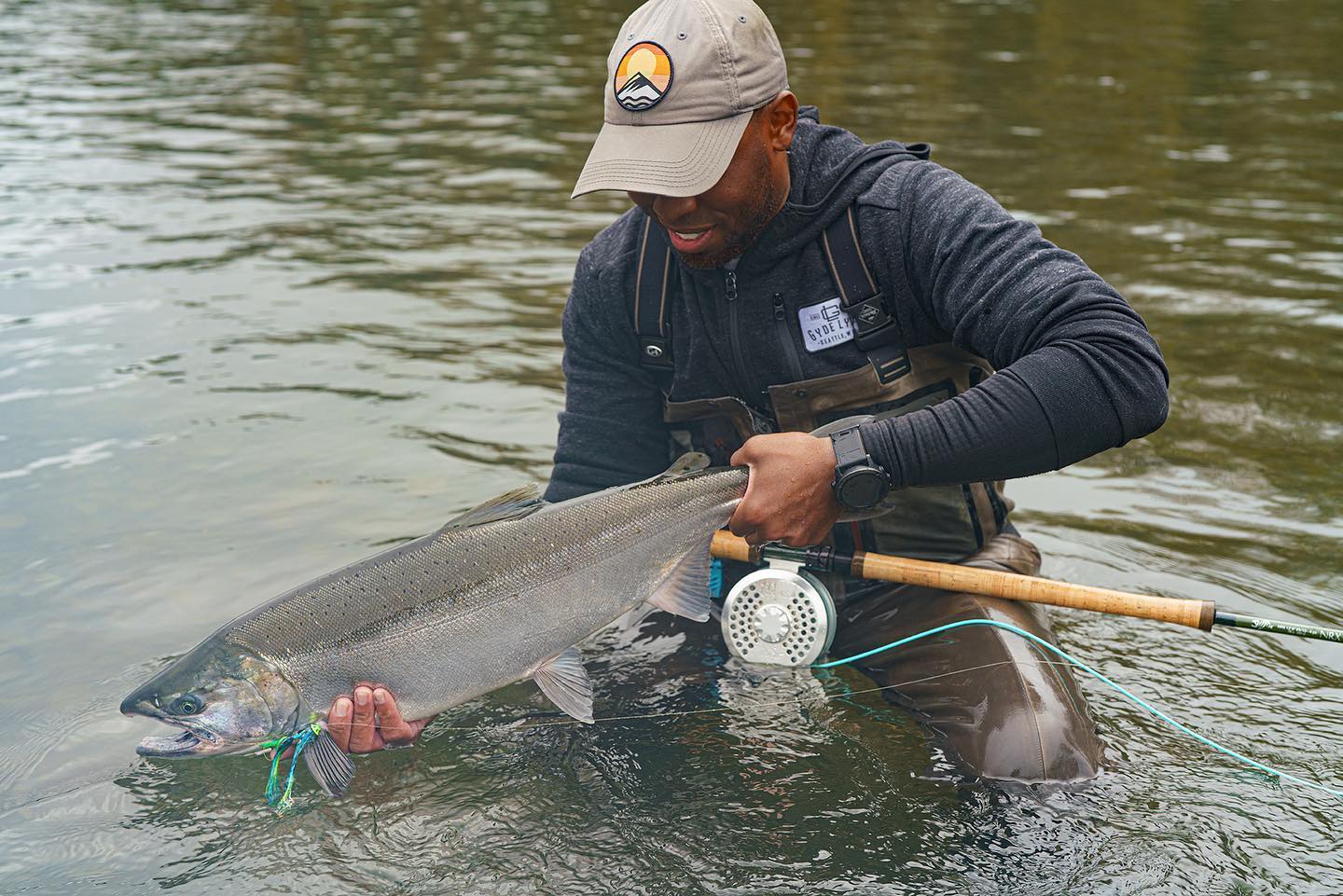 A man fishing stands in the water with a fish and fishing rod in hand.